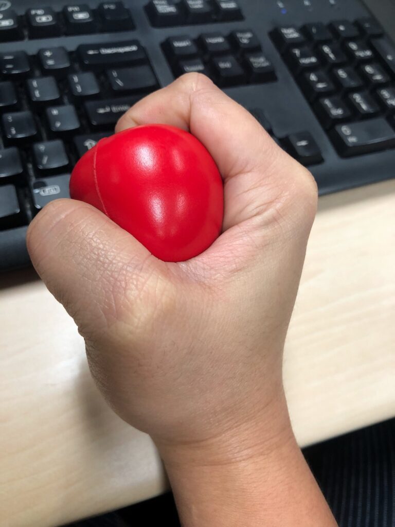 A hand squeezing a stress ball while at work in the office to manage emotional stress.