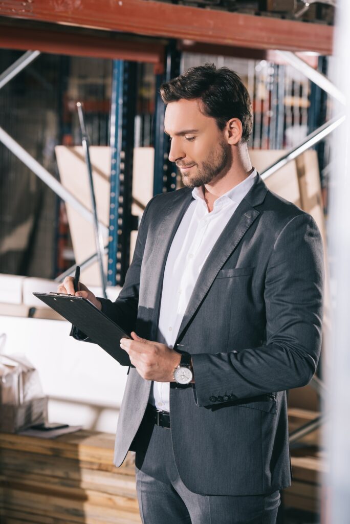 concentrated businessman writing on clipboard in warehouse