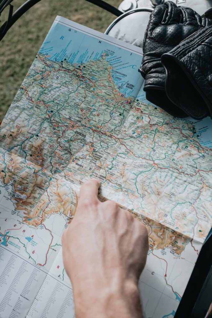 Hand pointing a place in a map while doing a bike travel. Gloves near the map