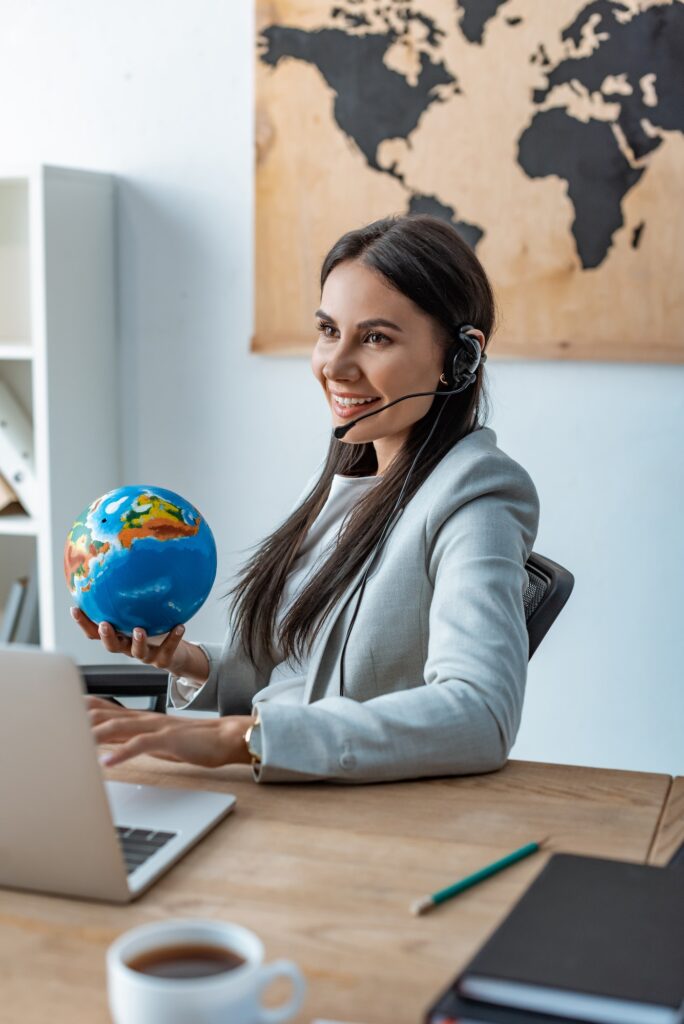 smiling travel agent holding globe while sitting at workplace
