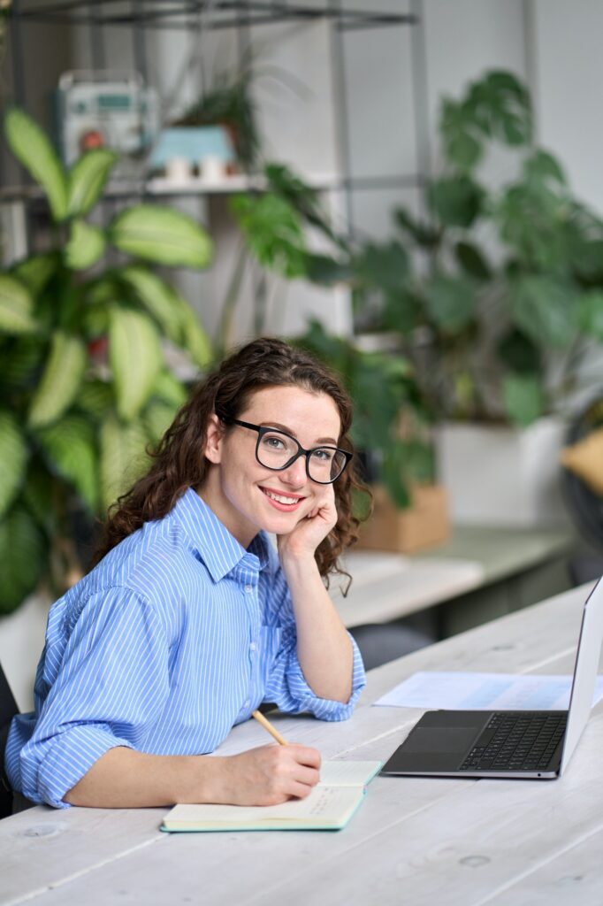 Young business woman working at desk with laptop. Vertical